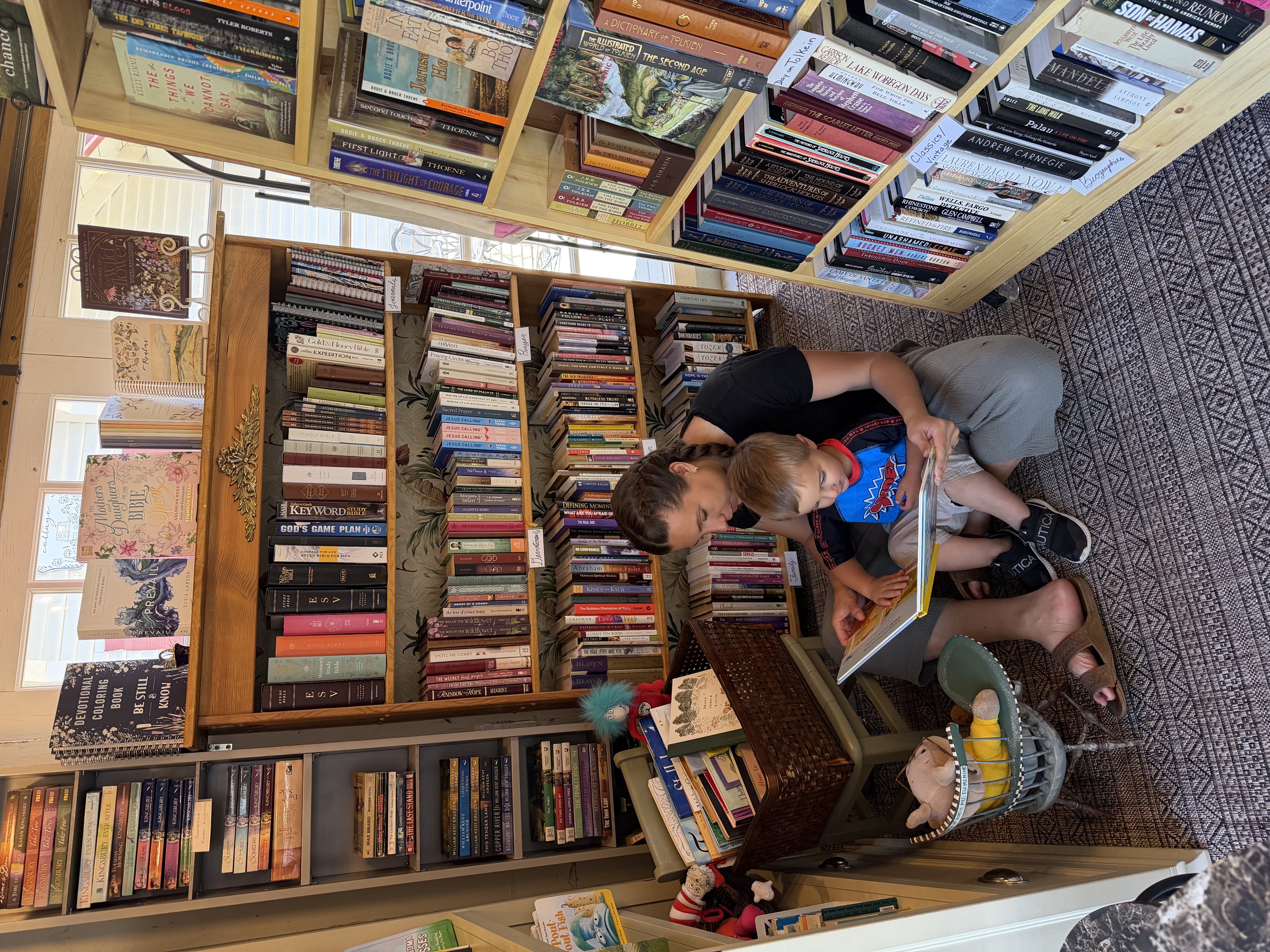 A parent and child sit on the bookstore rug reading a picture book together among the shelves
